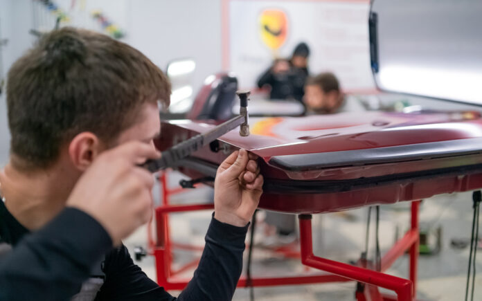 Karosár pracuje na odstránení preliačiny na aute špeciálnym náradím bez poškodenia laku